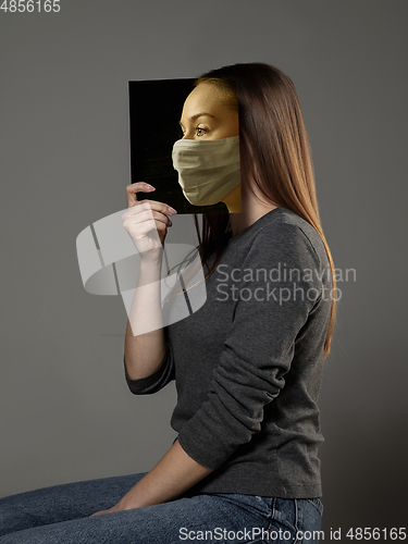 Image of Be safe and read to become someone else - woman covering face with book in face mask while reading on grey background