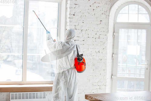 Image of Coronavirus Pandemic. A disinfector in a protective suit and mask sprays disinfectants in the house or office