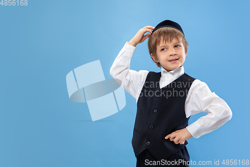 Image of Portrait of a young orthodox jewish boy isolated on blue studio background, meeting the Passover