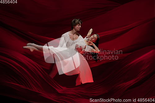 Image of Young and graceful ballet dancers on billowing red cloth background in classic action. Art, motion, action, flexibility, inspiration concept.