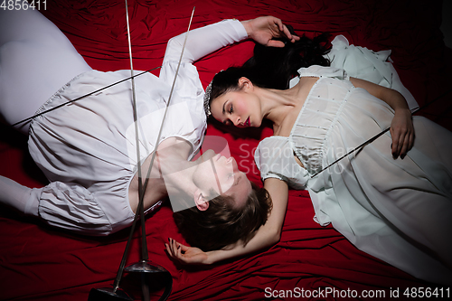 Image of Young and graceful ballet dancers on billowing red cloth background in classic action. Art, motion, action, flexibility, inspiration concept.
