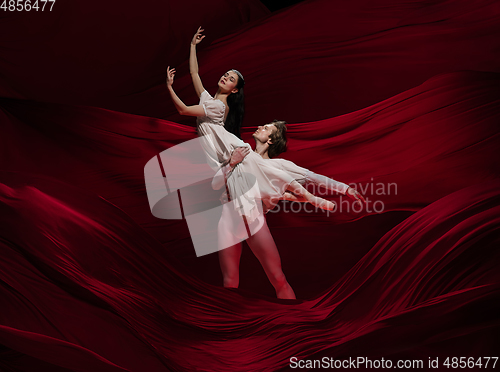 Image of Young and graceful ballet dancers on billowing red cloth background in classic action. Art, motion, action, flexibility, inspiration concept.