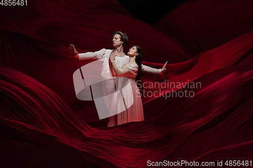 Image of Young and graceful ballet dancers on billowing red cloth background in classic action. Art, motion, action, flexibility, inspiration concept.