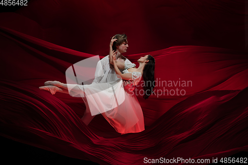 Image of Young and graceful ballet dancers on billowing red cloth background in classic action. Art, motion, action, flexibility, inspiration concept.