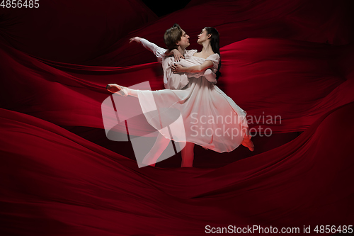 Image of Young and graceful ballet dancers on billowing red cloth background in classic action. Art, motion, action, flexibility, inspiration concept.