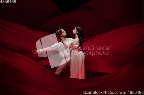 Image of Young and graceful ballet dancers on billowing red cloth background in classic action. Art, motion, action, flexibility, inspiration concept.