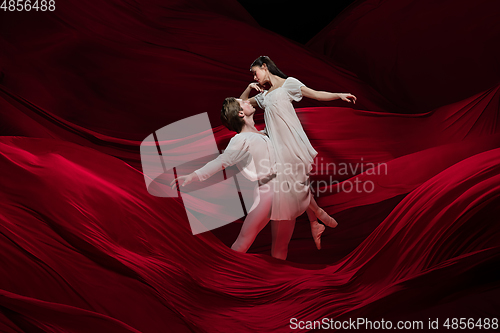 Image of Young and graceful ballet dancers on billowing red cloth background in classic action. Art, motion, action, flexibility, inspiration concept.