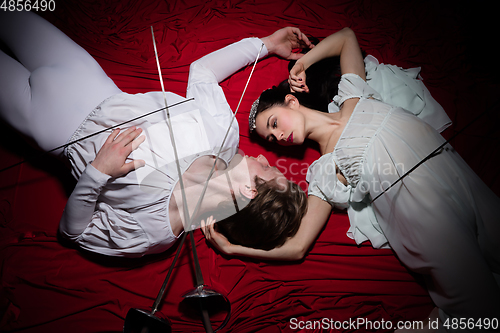 Image of Young and graceful ballet dancers on billowing red cloth background in classic action. Art, motion, action, flexibility, inspiration concept.