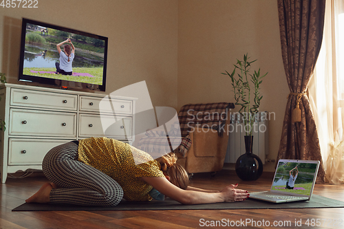 Image of Sporty young woman taking yoga lessons online and practice at home while being quarantine
