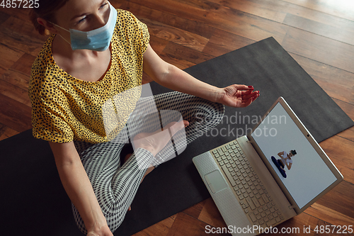 Image of Sporty young woman taking yoga lessons online and practice at home while being quarantine