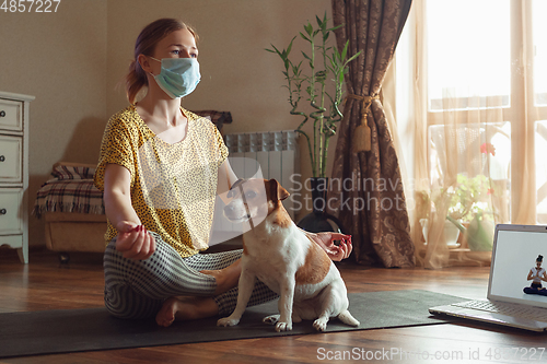 Image of Sporty young woman taking yoga lessons online and practice at home while being quarantine