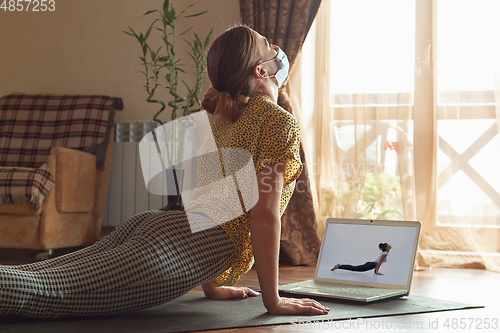 Image of Sporty young woman taking yoga lessons online and practice at home while being quarantine