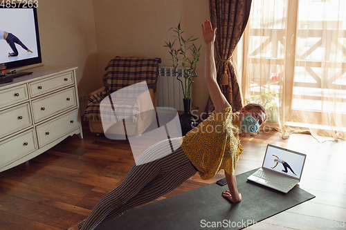 Image of Sporty young woman taking yoga lessons online and practice at home while being quarantine