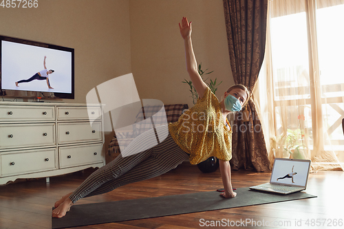 Image of Sporty young woman taking yoga lessons online and practice at home while being quarantine