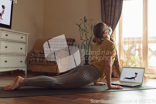 Image of Sporty young woman taking yoga lessons online and practice at home while being quarantine