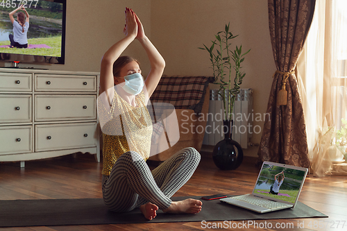 Image of Sporty young woman taking yoga lessons online and practice at home while being quarantine