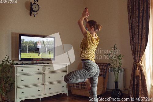 Image of Sporty young woman taking yoga lessons online and practice at home while being quarantine