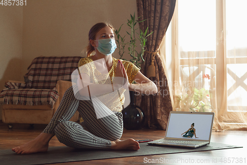 Image of Sporty young woman taking yoga lessons online and practice at home while being quarantine
