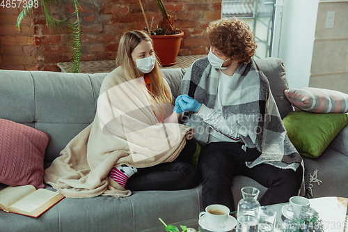 Image of Woman and man, couple in protective masks and gloves isolated at home with coronavirus symptoms