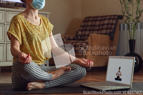 Image of Sporty young woman taking yoga lessons online and practice at home while being quarantine