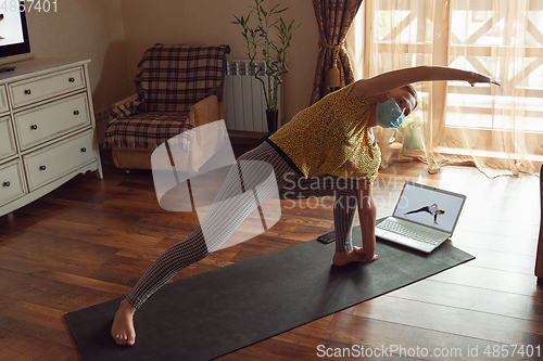 Image of Sporty young woman taking yoga lessons online and practice at home while being quarantine