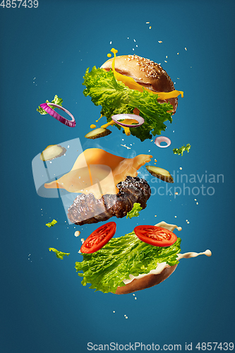 Image of Hamburger with flying ingredients on blue studio background. Fast food, cuisine concept.