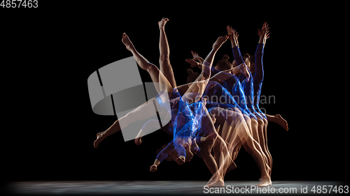 Image of Young flexible girl on black studio background in strobe and neon light. Young female model practicing artistic gymnastics.