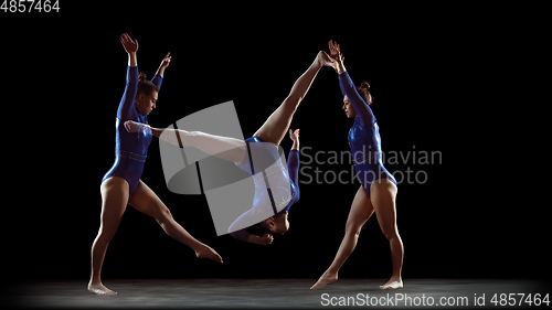 Image of Young flexible girl on black studio background in strobe and neon light. Young female model practicing artistic gymnastics.