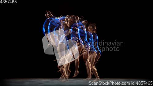 Image of Young flexible girl on black studio background in strobe and neon light. Young female model practicing artistic gymnastics.