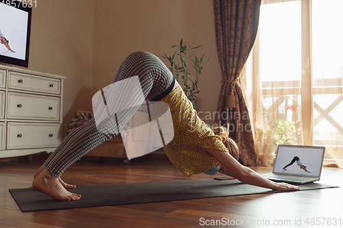 Image of Sporty young woman taking yoga lessons online and practice at home while being quarantine