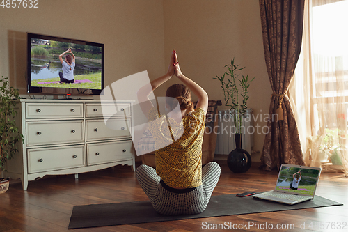 Image of Sporty young woman taking yoga lessons online and practice at home while being quarantine