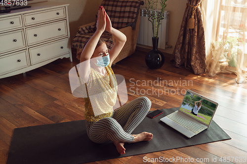 Image of Sporty young woman taking yoga lessons online and practice at home while being quarantine