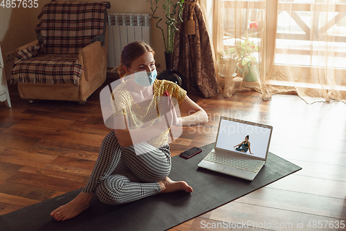 Image of Sporty young woman taking yoga lessons online and practice at home while being quarantine