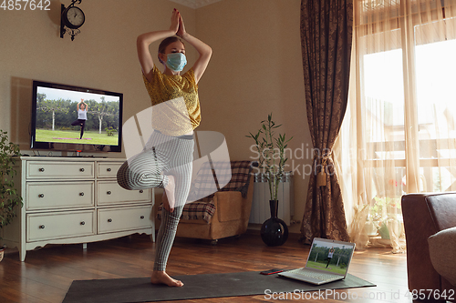 Image of Sporty young woman taking yoga lessons online and practice at home while being quarantine