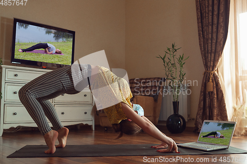 Image of Sporty young woman taking yoga lessons online and practice at home while being quarantine