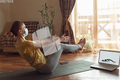 Image of Sporty young woman taking yoga lessons online and practice at home while being quarantine