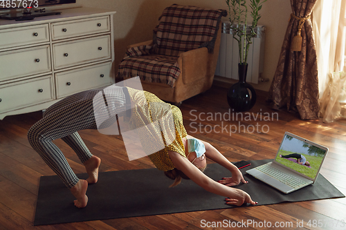 Image of Sporty young woman taking yoga lessons online and practice at home while being quarantine