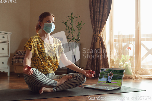 Image of Sporty young woman taking yoga lessons online and practice at home while being quarantine