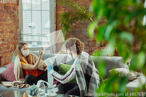 Image of Woman and man, couple in protective masks and gloves isolated at home with coronavirus symptoms