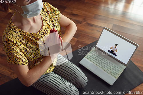 Image of Sporty young woman taking yoga lessons online and practice at home while being quarantine