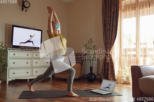 Image of Sporty young woman taking yoga lessons online and practice at home while being quarantine