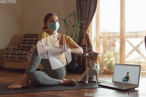 Image of Sporty young woman taking yoga lessons online and practice at home while being quarantine