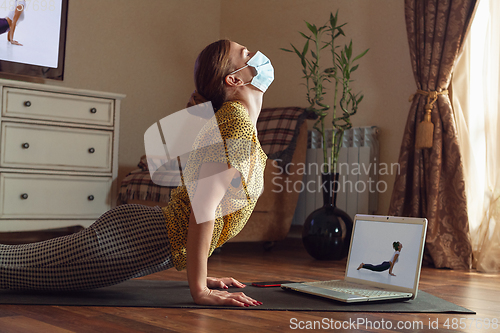 Image of Sporty young woman taking yoga lessons online and practice at home while being quarantine