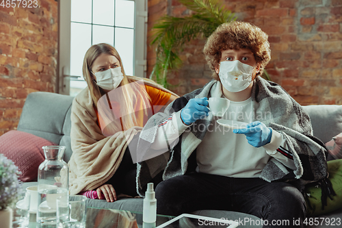 Image of Woman and man, couple in protective masks and gloves isolated at home with coronavirus symptoms