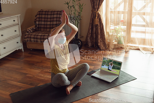 Image of Sporty young woman taking yoga lessons online and practice at home while being quarantine