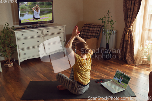 Image of Sporty young woman taking yoga lessons online and practice at home while being quarantine