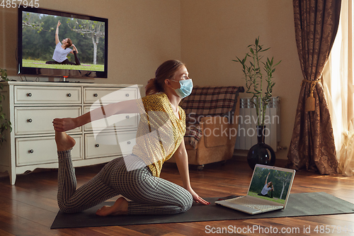 Image of Sporty young woman taking yoga lessons online and practice at home while being quarantine