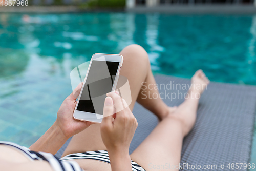 Image of Woman enjoy sun bath and using mobile phone in swimming pool