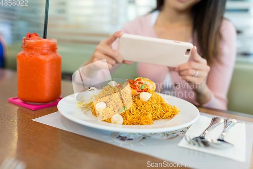 Image of Woman taking photo on fried noodles with cellphone