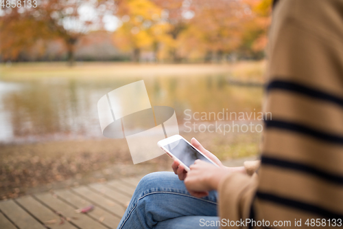 Image of Woman using cellphone in park at Autumn season